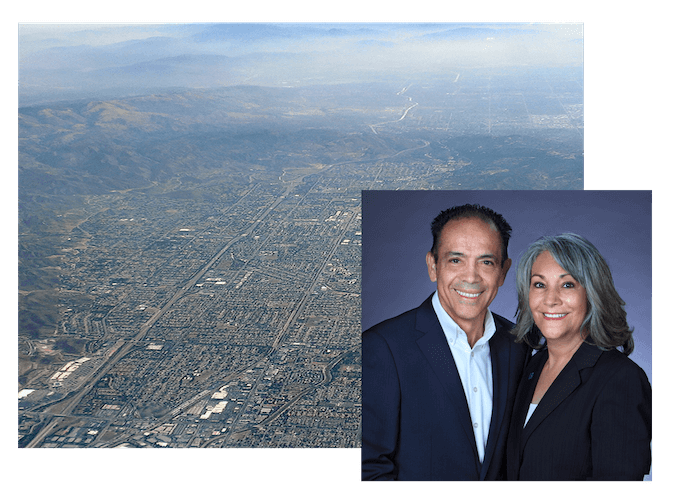 Two people standing in front of an aerial view of a city, with a focus on real estate.