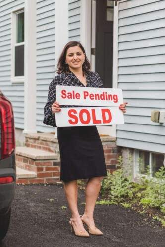 A woman standing in front of a car holding a real estate sale pending sign in Simi Valley.