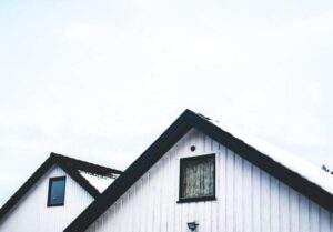 Two white wooden houses with dark roofs against a cloudy sky and a light dusting of snow.