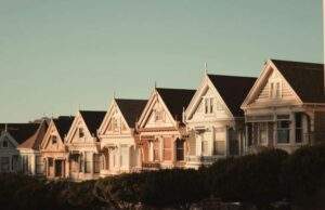 Row of Victorian-style houses under a clear sky, with trees partially visible in the foreground.