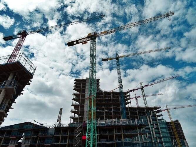 Construction site with multiple cranes and partially built high-rise buildings against a cloudy sky.