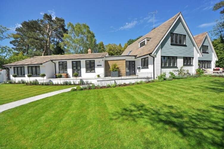 A spacious suburban house with a large, well-maintained lawn and a path leading to the entrance, set under a clear blue sky.