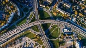 Aerial view of a complex highway interchange with multiple lanes, surrounded by green spaces and residential buildings.