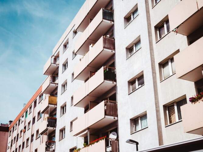 A multi-story residential building with several balconies, seen from an angle under a clear blue sky.