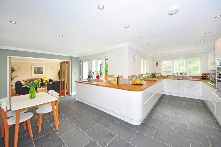 A spacious kitchen with white cabinets, wooden countertops, and gray tiled floor. A dining table with four chairs and a vase of flowers is in the corner.